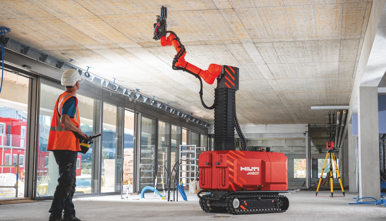 Pracownicy budowlani bezpiecznie obsługujący robota Jaibot do wierceń nad głową na placu budowy