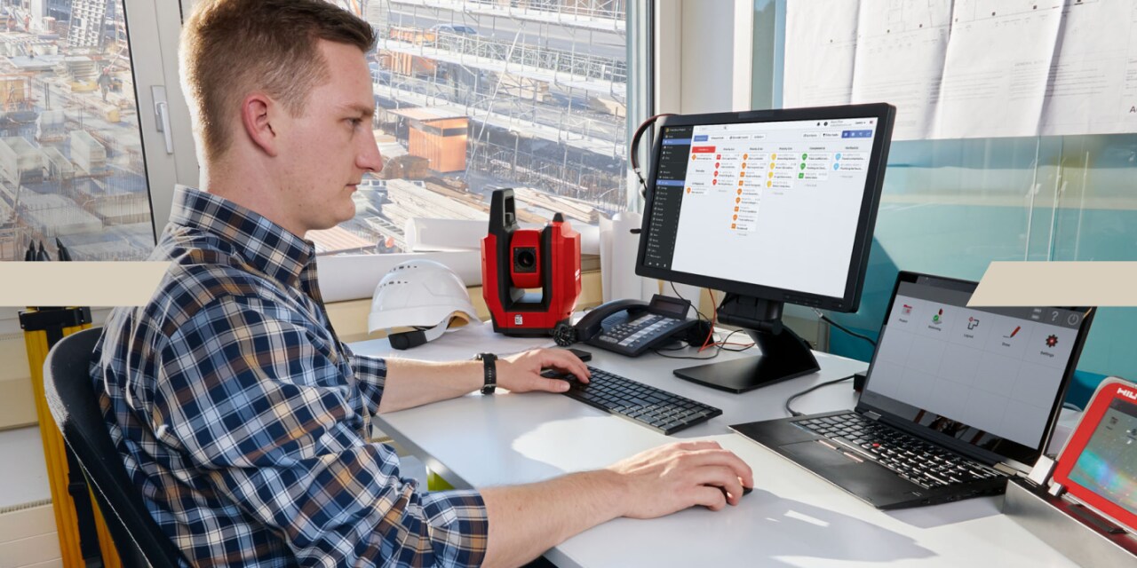 Mężczyzna siedzi przed komputerem w biurze, pracuje, na ekranie wyświetlany jest program Fieldwire.