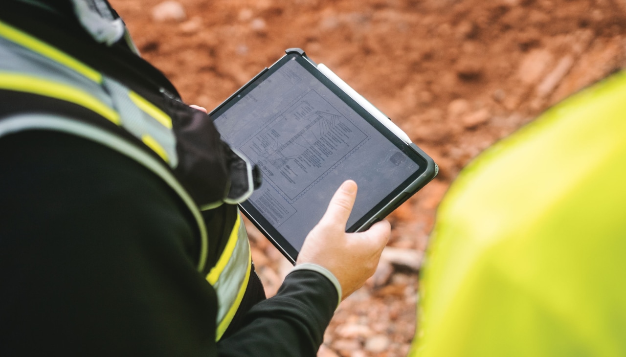 Zbliżenie na tablet trzymany przez osobę ubraną w odzież budowlaną.