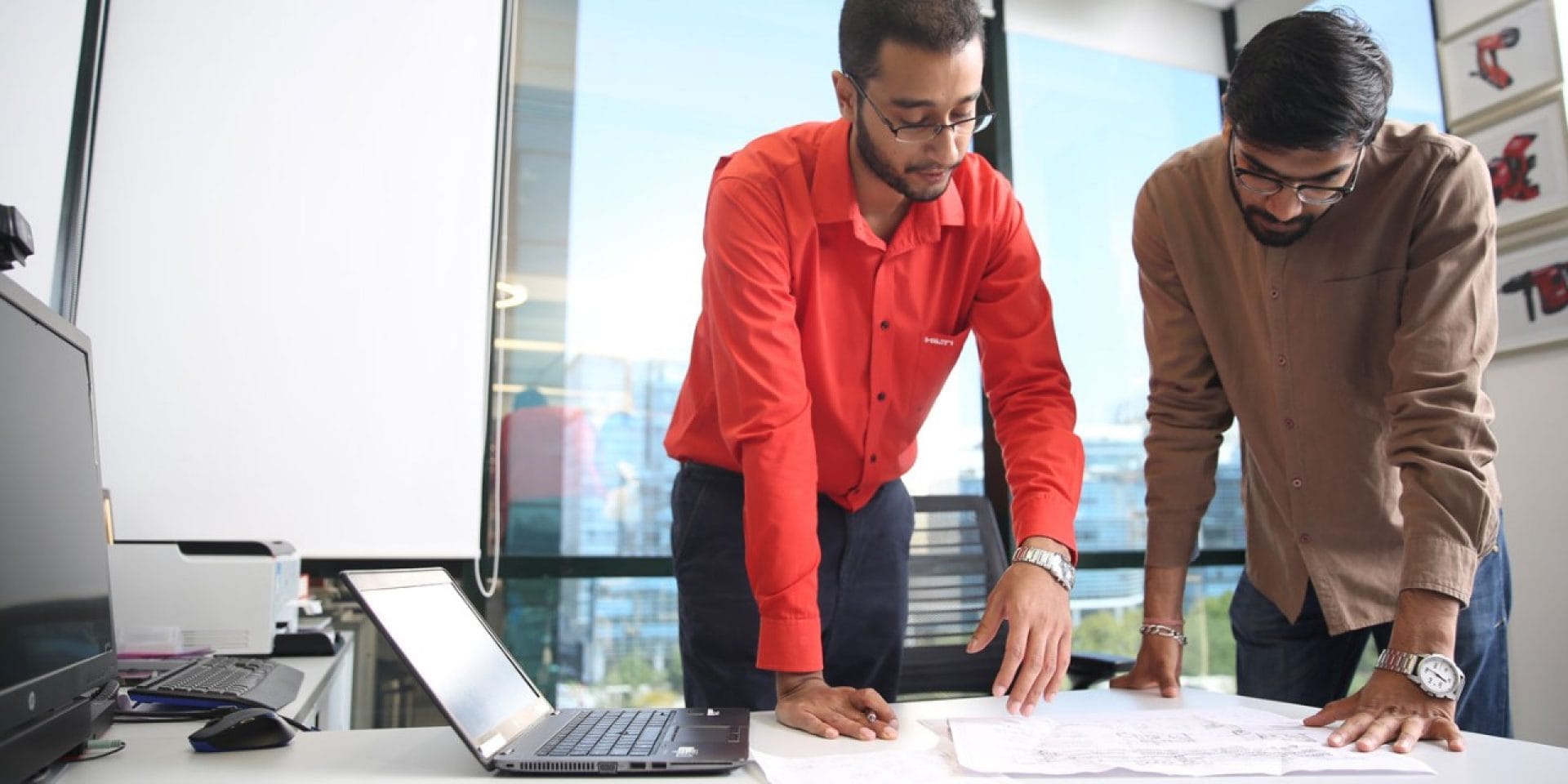 A Hilti engineer with a customer  standing at a desk looking  at a plan